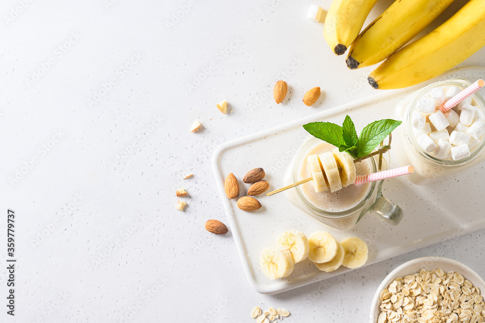 Banana milkshake with oatmeal and almond nuts in mason jar on white board. View from above. Space for text. Banana milkshake with oatmeal and almond nuts in mason jar on white board. View from above. Space for text.