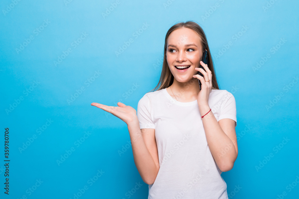 Young woman talking on the phone with open palm on a blue background Young woman talking on the phone with open palm on a blue background
