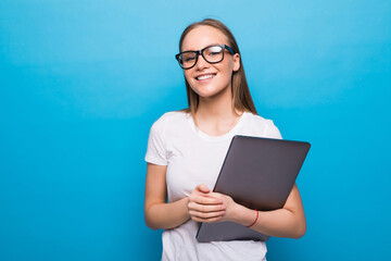 Young studing holding her laptop in her arms on blue background