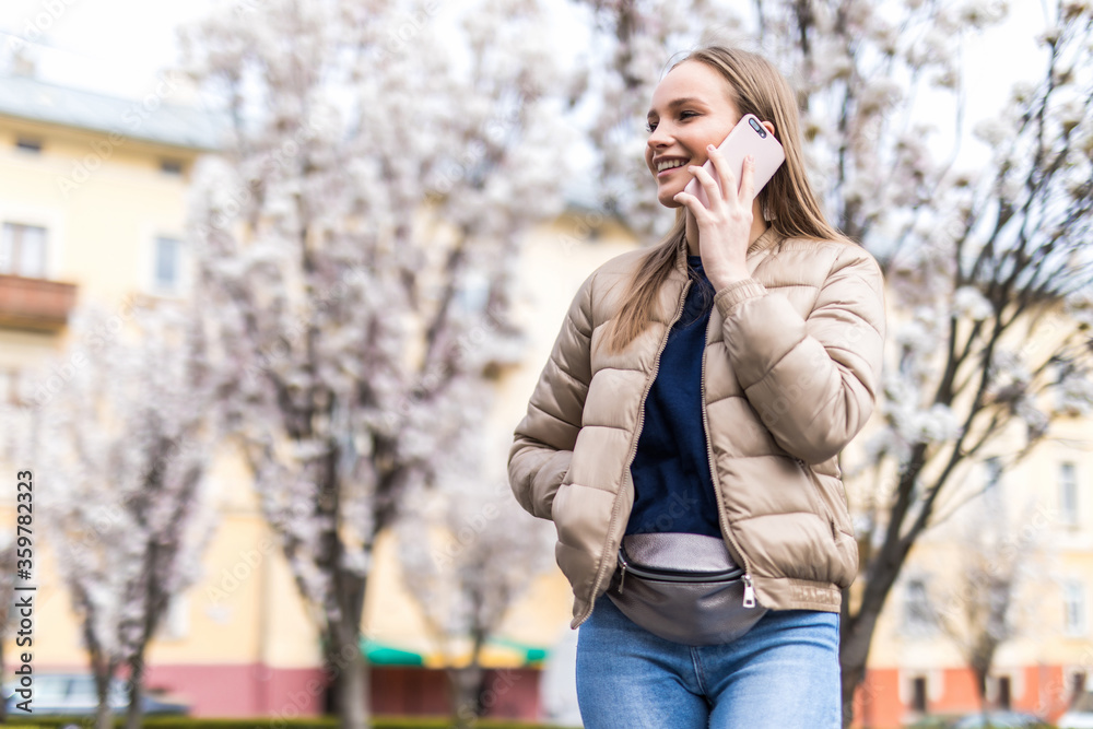 Fototapeta premium Beautiful woman talking with smartphone on Sakura or cherry blossom background