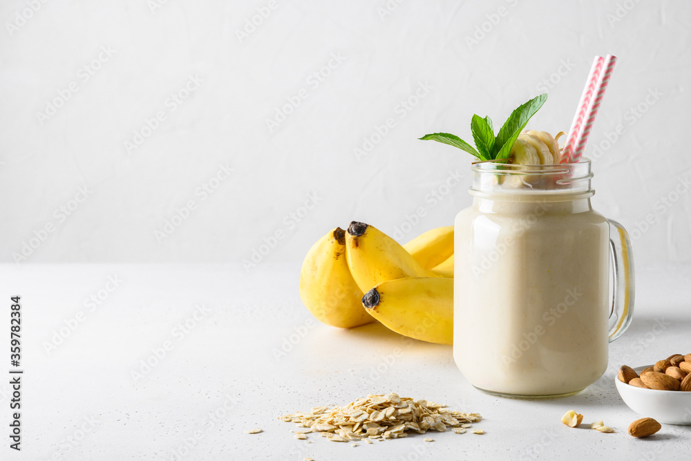 Banana milkshake with oatmeal and almond nuts in mason jar on white board. Space for text. - obrazy, fototapety, plakaty 