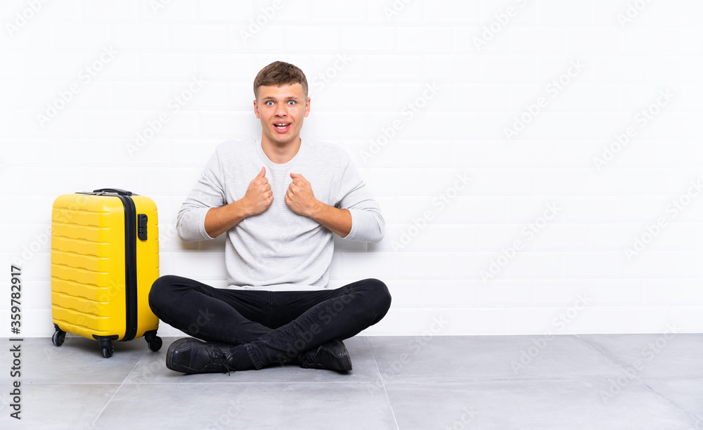 Young handsome man sitting on the floor with a suitcase celebrating a victory Young handsome man sitting on the floor with a suitcase celebrating a victory