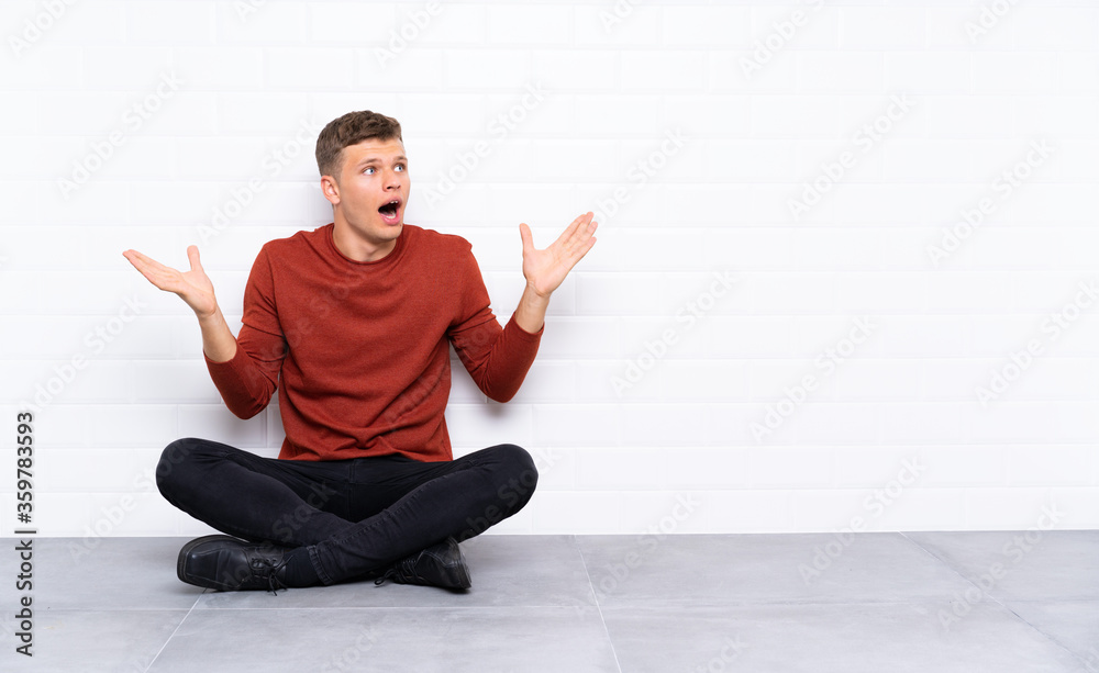 Young handsome man sitting on the floor with surprise facial expression
