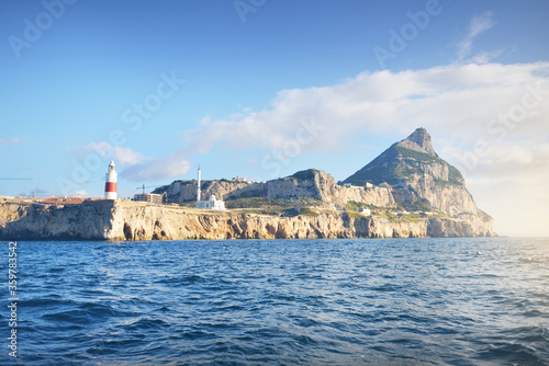 Trinity lighthouse at the rocky shore (cliffs) of the Europa Point. British Overseas Territory of Gibraltar, Mediterranean sea.A view from the yacht. National landmark, sightseeing, travel destination