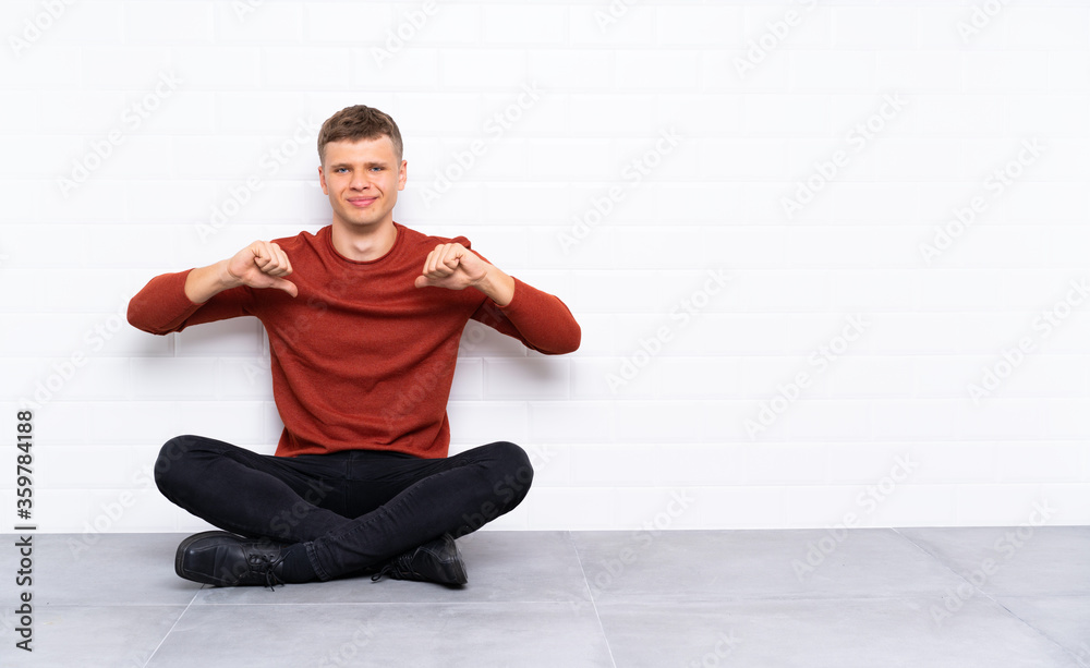 Fototapeta premium Young handsome man sitting on the floor proud and self-satisfied