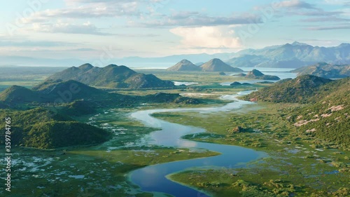 Blue river flowing through green valley toward distant mountains. Bends and curves of Crnojevica river in Montenegro, meandering through the marsh among hills on its way to lake Skadar. Aerial footage
