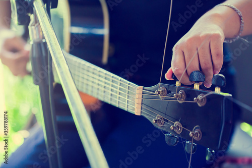 Selectice to hand guitarist adjusting pegs on acoustic guitar during music lesson at home. Woman singer adjusting strings for better playing on acoustic guitar. String musical instrument concept. photo