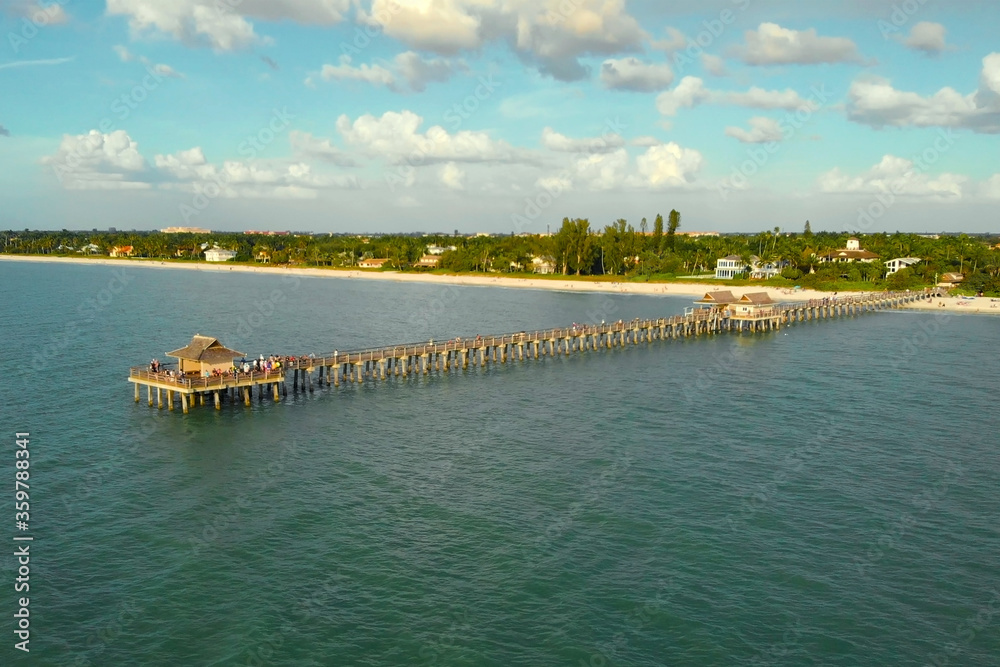 Drone flies near a pier in Naples, Florida at sunset time, aerial view. Drone flies around a fishing pier in Naples, Florida USA. Long wooden pier at sea. Ocean fishing pier, aerial view.