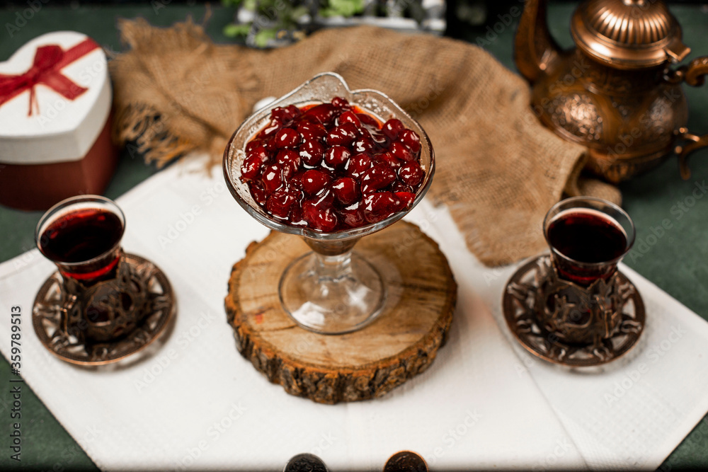 Cherry confiture in a glass jar on a piece of wood with two glasses of tea