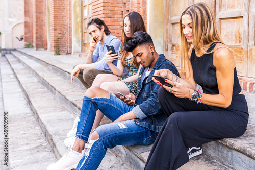 group of multiracial friends sitting on a marble staircase using smartphones