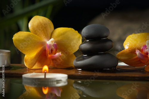 Black zen stones  candles and yellow orchids on a wooden plank on the surface of the water. SPA  relaxation  meditation concept