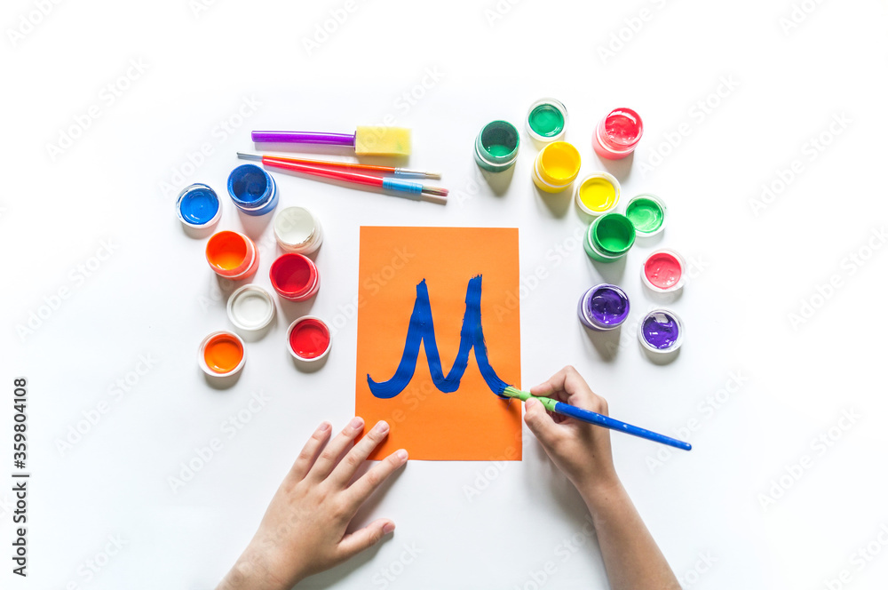 Children's hands write the letter M gouache paint Children's hands write the letter M gouache paint