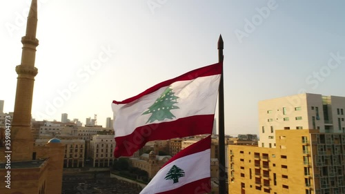 Beirut, Lebanon 2019: sunset turn around right slow motion drone shot on Lebanese flag with mosque, church and sun flaring in the background during the Lebanese revolution photo