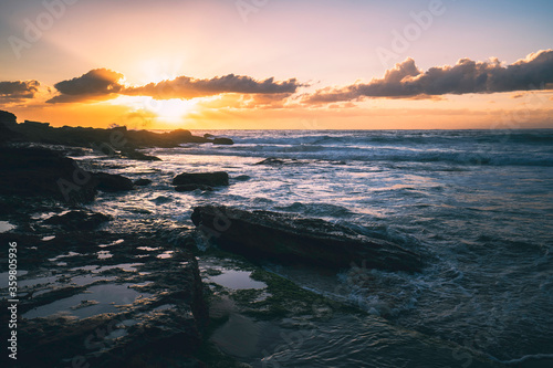 sunset over the sea, waves crashing on rocks at the beach
