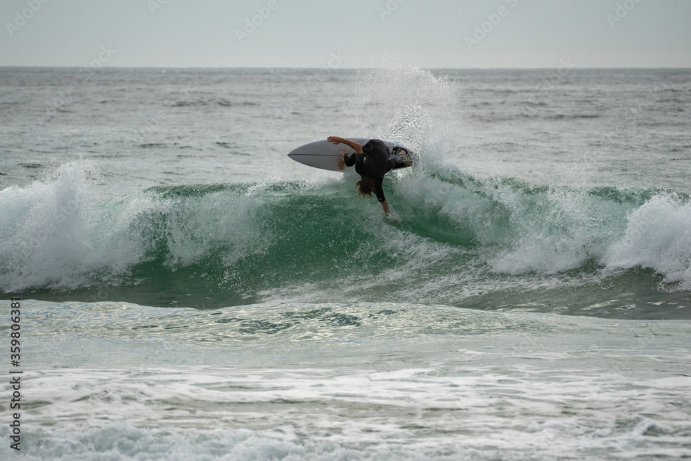 Young male surfer catching a wave and doing a big turn on it at Manly beach in Australia, craving, tricks, splash, wave, catching waves