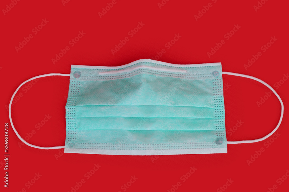 Surgical face mask with rubber ear straps on red background. Protection concept. Medical equipment