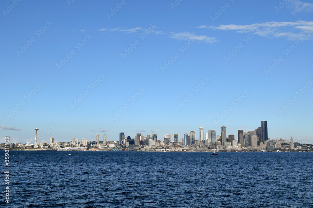 View of Seattle from Alki Beach in West Seattle over the Puget Sound; wide panoramic view of the city with a few small boats in between on the water.