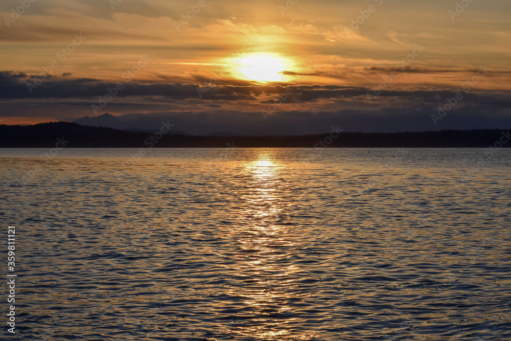 Bright sunset with dramatic clouds over Olympic Peninsula viewed from Alki Beach in West Seattle. Bright sunset with dramatic clouds over Olympic Peninsula viewed from Alki Beach in West Seattle.