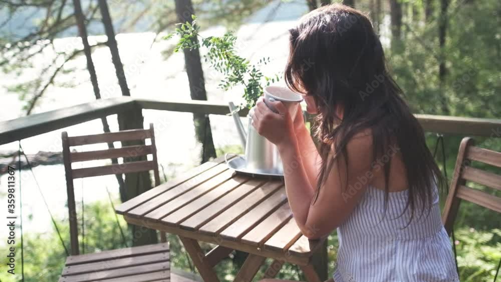 Attractive brunette girl with a cup of tea or coffee in her hands enjoys nature in the mountains sitting on the balcony. young woman is enjoying coffee on nature background. Attractive brunette girl with a cup of tea or coffee in her hands enjoys nature in the mountains sitting on the balcony. young woman is enjoying coffee on nature background.