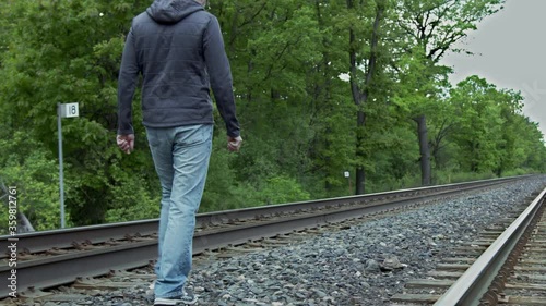 High quality 4k video of a young man who is walking on the railway away from the camera, focus on legs. Men wearing jeans and sport jacket.