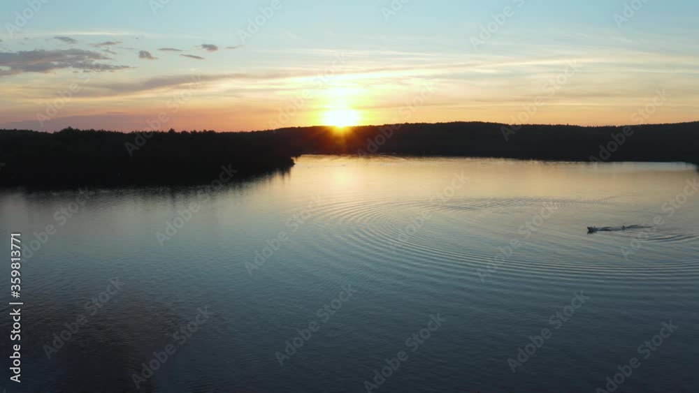 Drone shot over a beautiful sunset on a lake with a single boat waterskier in Quebec, Canada Drone shot over a beautiful sunset on a lake with a single boat waterskier in Quebec, Canada