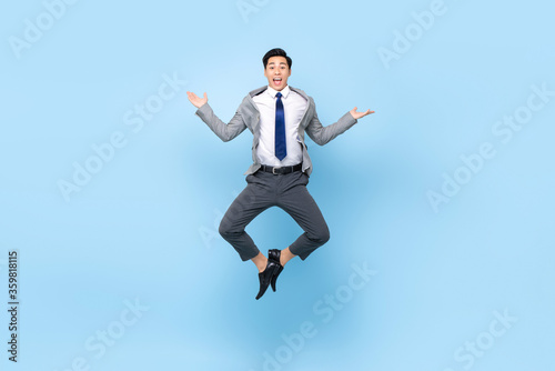 Wallpaper Mural Full length playful portrait of happy ecstatic young Asian businessman jumping in mid-air doing wacky fun gesture in isolated studio blue background Torontodigital.ca