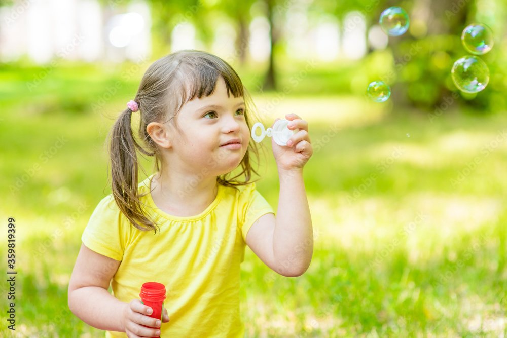Happy little girl with syndrome down blows bubbles in a summer park Happy little girl with syndrome down blows bubbles in a summer park