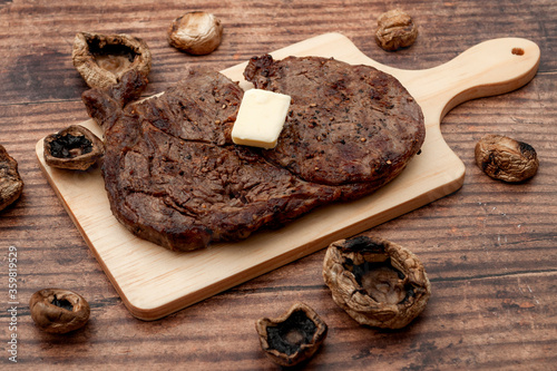 Rustic dining and healthy meat concept with photograph of tender beef steak, stick of butter and grilled mushrooms isolated on dark wood background