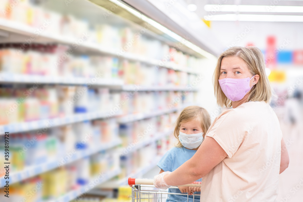 Portrait of a mother and her little daughter wearing protective face mask at a supermarket during the coronavirus epidemic or flu outbreak. Empty space for text