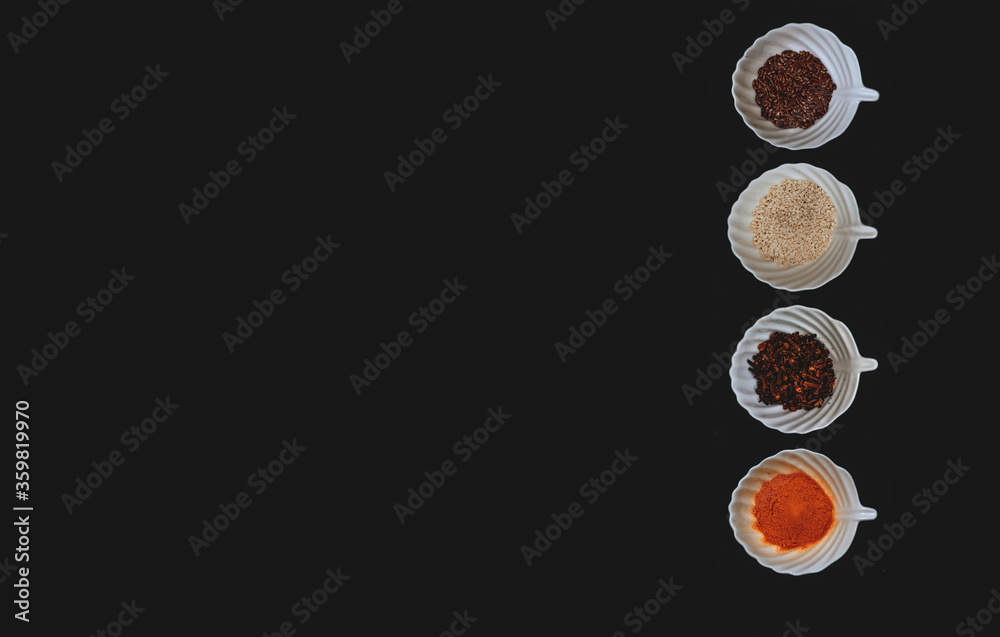 Fototapeta premium A border of spices and grains in white cups on a black isolated background. Top view