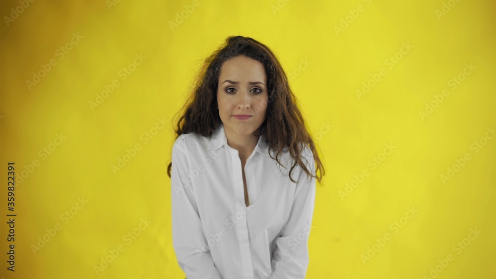 Guilty young beautiful woman in shirt standing in hesitation on yellow background Guilty young beautiful woman in shirt standing in hesitation on yellow background