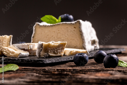 French goat Valencay cheese. Pouligny-Saint-Pierre French cheese with blue mold with berries on a slate board rustic background