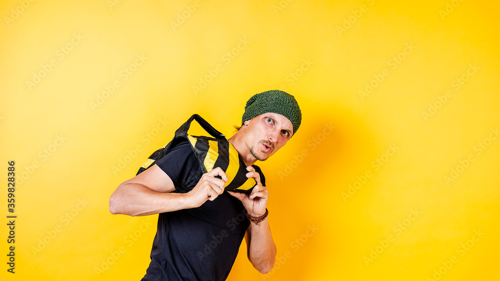 a white man on a yellow background holding a load of sand, a striped bag, a hipster in a hat a white man on a yellow background holding a load of sand, a striped bag, a hipster in a hat
