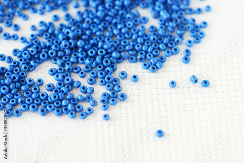 Blue seed beads scattered on a white textile background closeup. Handmade concept