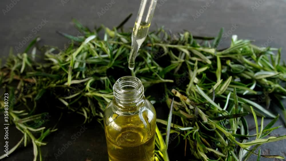 Dripping of fresh rosemary oil into bottle on dark background, closeup Dripping of fresh rosemary oil into bottle on dark background, closeup