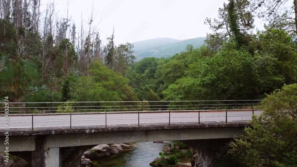 Aerial shot crossing above asphalt car bridge at Oitaven river, Aranza. Galicia Spain. Wild forest shot with mountains at the background Aerial shot crossing above asphalt car bridge at Oitaven river, Aranza. Galicia Spain. Wild forest shot with mountains at the background