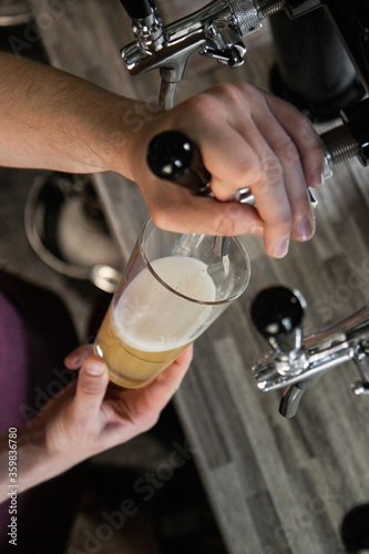man at the bar pours beer into a glass on a wooden table background