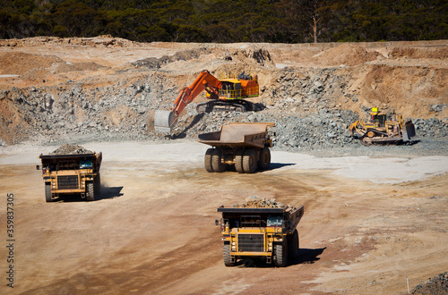 Large yellow trucks used in modern mine Western Australia. Bulldozer moves rock towards digger which fills trucks which transport ore from the open cast mine. photo