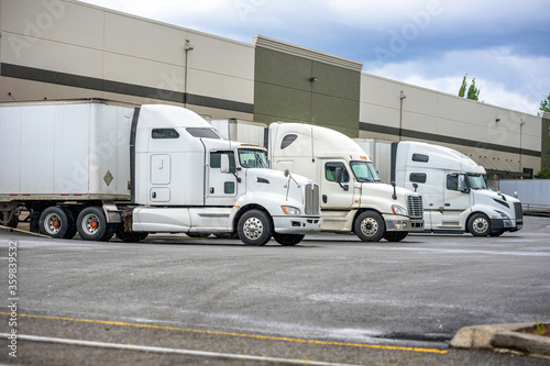 Fototapet Different models of big rigs semi trucks with dry van semi trailers loading carg
