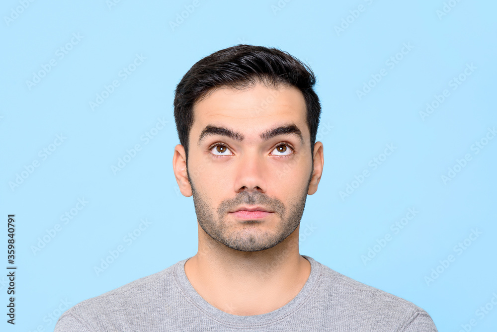 Obraz premium Close up portrait of serious handsome Caucasian man thinking while looking up in isolated studio blue background