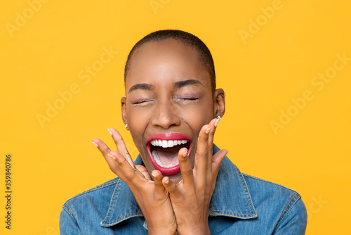 Close up portrait of ecstatic young African American woman screaming with hands covering face isolated studio yellow background photo