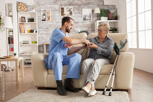 Male nurse using digital blood pressure device on senior woman in nursing home.