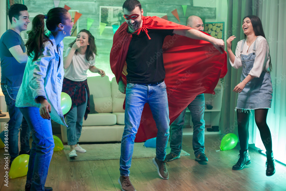Obraz premium Caucasian man wearing superhero costume jumping in the air at friends party.