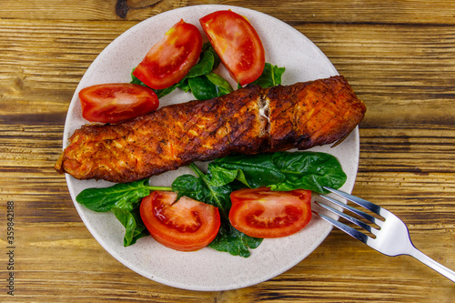 Grilled salmon fillet with spinach and tomatoes on wooden table. Top view
