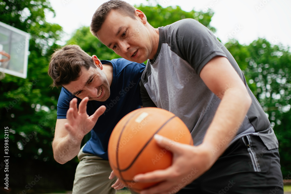 Two young men playing basketball in the park. Friends having a friendly match outdoors	