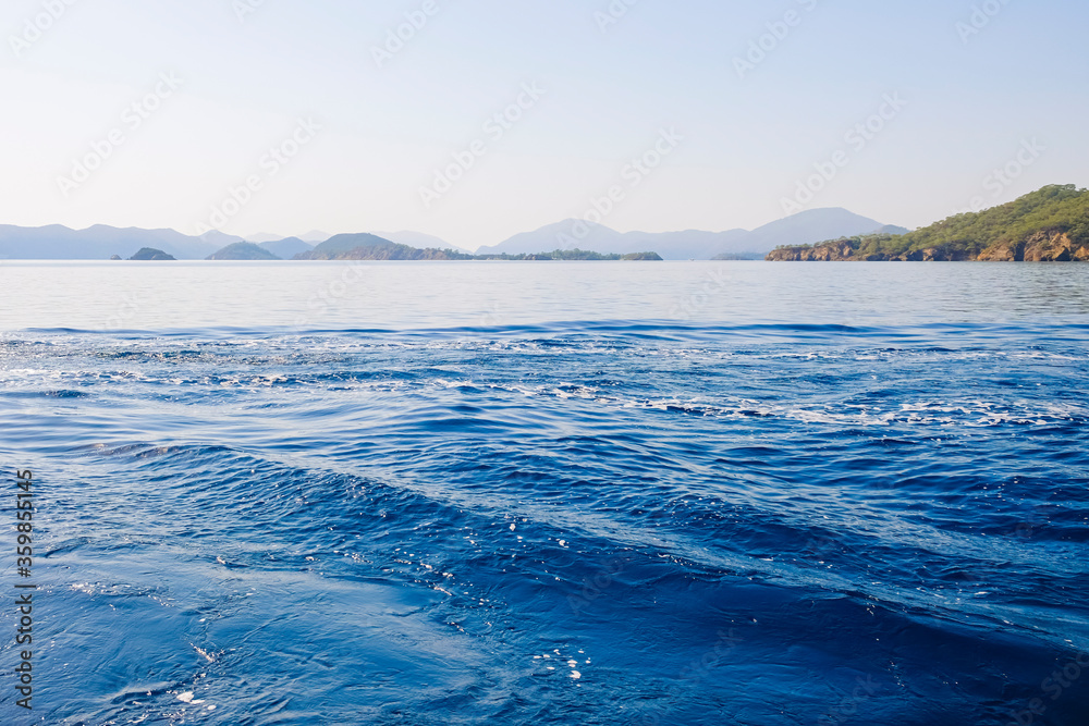 Peaceful seascape. Beautiful blue sky over calm sea with sunlight reflection. Sea waves. Mountains on horizon.