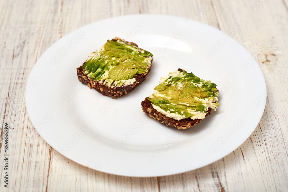 Slice of cereal bread with cream cheese and avocado on a white plate. Vegetarian sandwich. Slice of cereal bread with cream cheese and avocado on a white plate. Vegetarian sandwich.