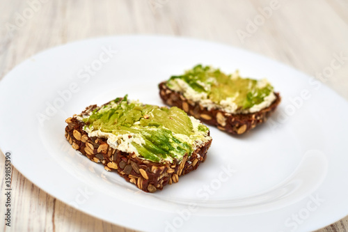 Slice of cereal bread with cream cheese and avocado on a white plate. Vegetarian sandwich.