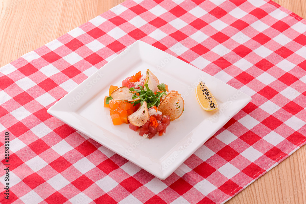 Plate of traditional Caesar Salad with chicken and salad on light wooden table with plaid tablecloth.