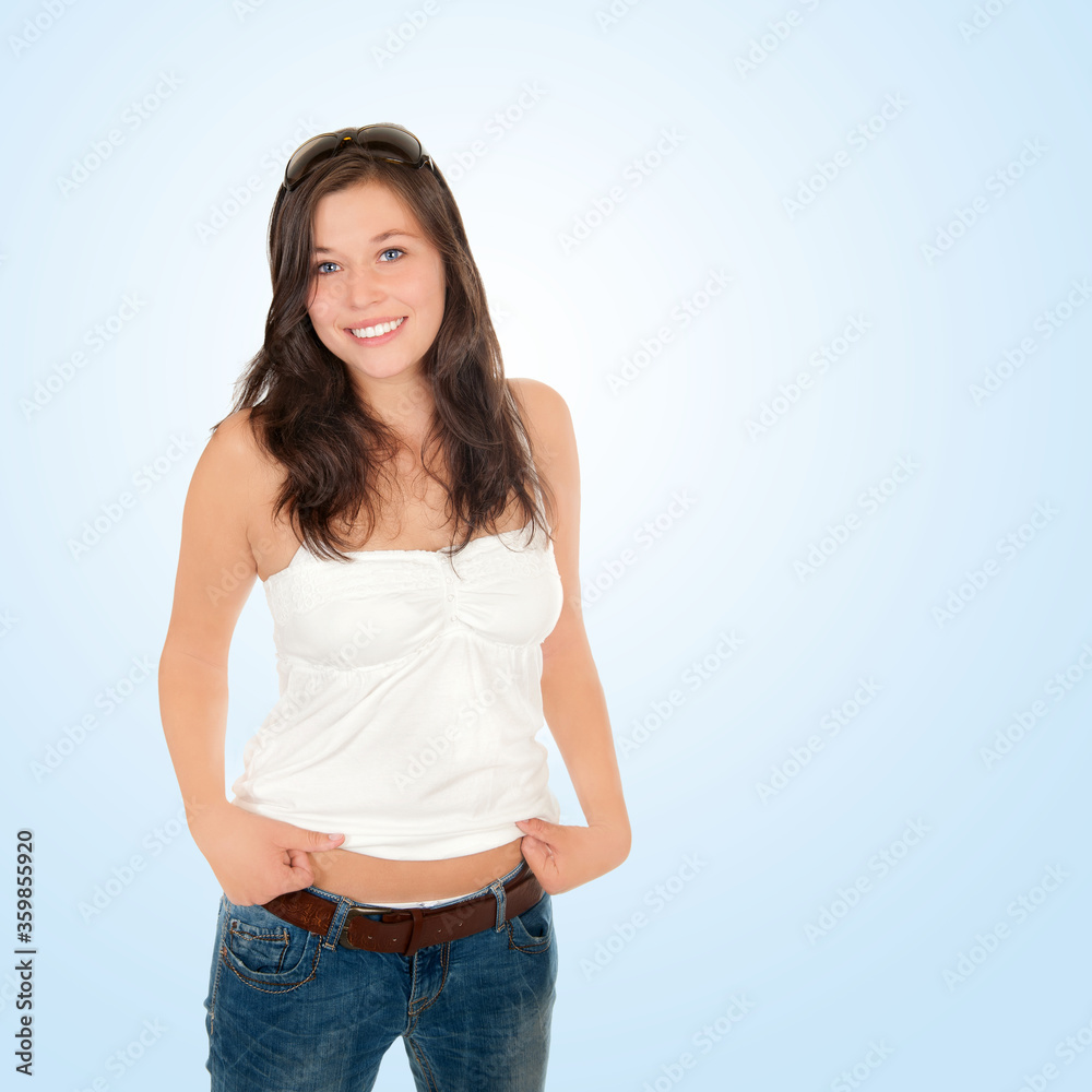 Fototapeta premium Closeup portrait of a beautiful girl wearing sunglasses, blue jeans and white top in front of blue background